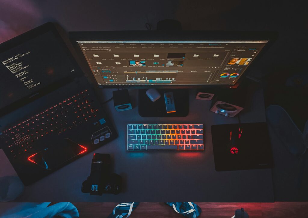 A contemporary workspace featuring dual monitors, a rainbow-lit keyboard, and editing software, perfect for tech enthusiasts.